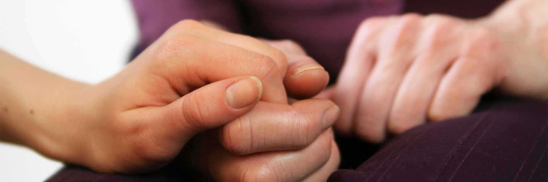 Foto: Die geröteten Hände einer Frau liegen sichtbar verkrampft auf ihrem Schoß. Eine andere Frau hält ihre Hand.