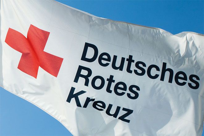 Foto: Eine Fahne des Deutschen Roten Kreuzes weht unter strahlend blauem Himmel.